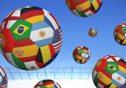 Multiple soccer balls decorated with international flags, including Brazil, Argentina, and the USA, float above a stadium with a blue sky—an iconic scene perfect for a sports and entertainment marketing agency campaign.